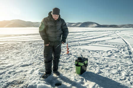A fisherman is fishing in a hole on the ice of a large frozen lake on a sunny day. The joy of winter fishing on Lake Baikalの写真素材