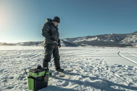 A fisherman is fishing in a hole on the ice of a large frozen lake on a sunny day. The joy of winter fishing on Lake Baikalの写真素材