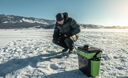 A fisherman is fishing in a hole on the ice of a large frozen lake on a sunny day. The joy of winter fishing on Lake Baikalの写真素材