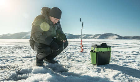 A fisherman is fishing in a hole on the ice of a large frozen lake on a sunny day. The joy of winter fishing on Lake Baikalの写真素材