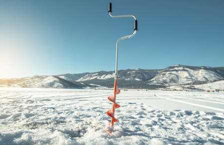 A drill for winter fishing is screwed into the ice of a large lake on a sunny day. winter fishing conceptの写真素材