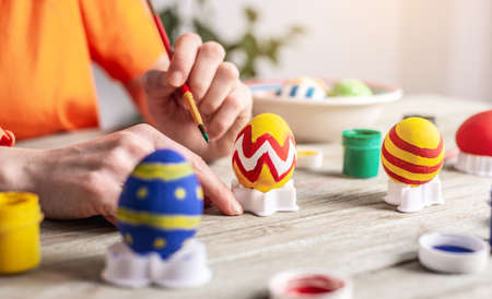 Woman's hand with a brush is drawing a colored pattern on an Easter egg. Preparation for the bright Easter holiday.の写真素材