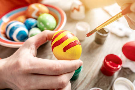 Hand with a brush is drawing a colored pattern on an Easter egg. Preparation for the bright Easter holiday.の写真素材
