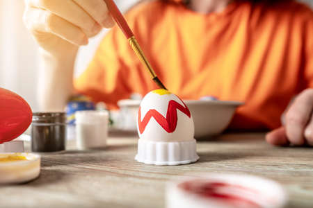 Woman's hand with a brush is drawing a colored pattern on an Easter egg. Creative preparation for bright Easter holidayの写真素材