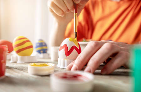 Woman's hand with a brush is drawing a colored pattern on an Easter egg. Creative preparation for bright Easter holidayの写真素材