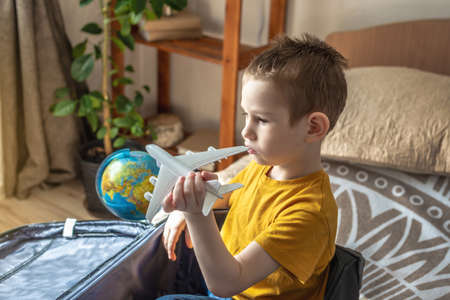A child boy in a yellow T-shirt is playing with a toy airplane and a globe of the earth. The concept of going on a journey towards adventure.の写真素材