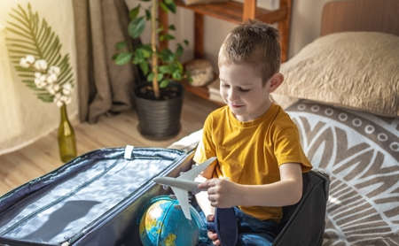 A child boy in a yellow T-shirt is playing with a toy airplane and a globe of the earth. The concept of going on a journey towards adventure.の写真素材