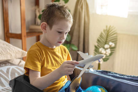 A child boy in a yellow T-shirt is playing with a toy airplane. The concept of going on a journey towards adventure.の写真素材