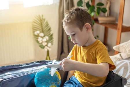 A child boy in a yellow T-shirt is playing with a toy airplane and a globe of the earth. The concept of going on a journey towards adventure.の写真素材