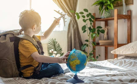 A child boy with a large backpack is playing with a toy airplane and a globe of the earth. The concept of going on a journey towards adventure.の写真素材