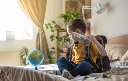 A child boy with a large backpack is playing with a toy airplane and a globe of the earth. The concept of going on a journey towards adventure.の写真素材
