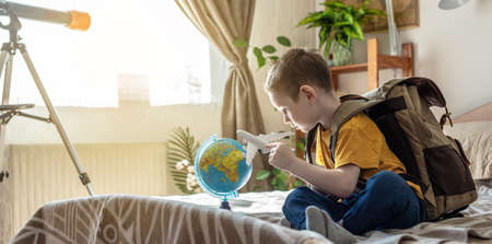 A child boy with a large backpack is playing with a toy airplane and a globe of the earth. The concept of going on a journey towards adventure.の写真素材