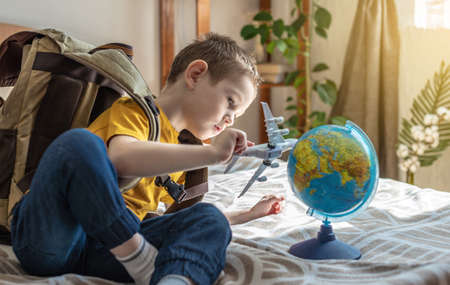 A child boy with a large backpack is playing with a toy airplane and a globe of the earth. The concept of going on a journey towards adventure.の写真素材