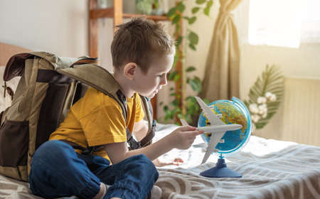 A child boy with a large backpack is playing with a toy airplane and a globe of the earth. The concept of going on a journey towards adventure.の写真素材