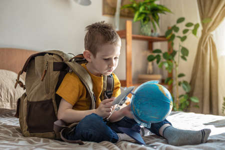A child boy with a large backpack is playing with a toy airplane and a globe of the earth. The concept of going on a journey towards adventure.の写真素材