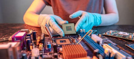 The engineer's gloved hand is holding the CPU chip against the background of the motherboard. Concept of high-tech hardware microelectronicsの写真素材