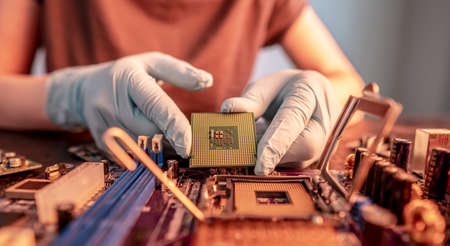 The engineer's gloved hand is holding the CPU chip against the background of the motherboard. Concept of high-tech hardware microelectronicsの写真素材