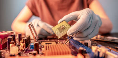 Engineer repairman holding hands in black gloves chip processor, CPU to insert into the socket of the computer motherboard. The concept of technology hardware in the neon lightの写真素材