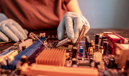 The engineer's gloved hand is holding the CPU chip against the background of the motherboard. Concept of high-tech hardware microelectronicsの写真素材
