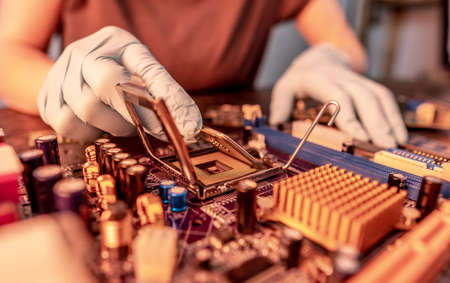 Engineer repairman holding hands in black gloves chip processor, CPU to insert into the socket of the computer motherboard. The concept of technology hardware in the neon lightの写真素材
