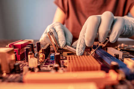 Engineer repairman holding hands in black gloves chip processor, CPU to insert into the socket of the computer motherboard. The concept of technology hardware in the neon lightの写真素材