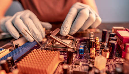 Engineer repairman holding hands in black gloves chip processor, CPU to insert into the socket of the computer motherboard. The concept of technology hardware in the neon lightの写真素材