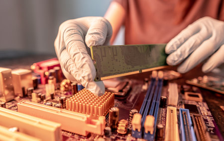 A repair engineer holds a RAM chip with his hands in black gloves, inserts the computer's RAM into the socket of the computer's motherboard. The concept of technological equipmentの写真素材