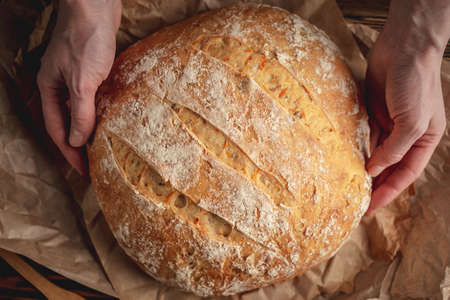 Female hands holding homemade natural fresh bread with a Golden crust on a napkin on an old wooden background . The concept of baking bakery productsの写真素材