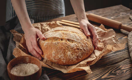 Female hands holding homemade natural fresh bread with a Golden crust on a napkin on an old wooden background . The concept of baking bakery productsの写真素材