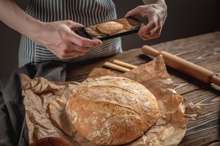 A baker is taking pictures of homemade fresh bread on his phone for a post on social networks. The concept of baking bakery productsの写真素材