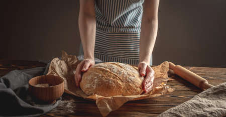 Female hands holding homemade natural fresh bread with a Golden crust on a napkin on an old wooden background . The concept of baking bakery products. rustic style.の写真素材