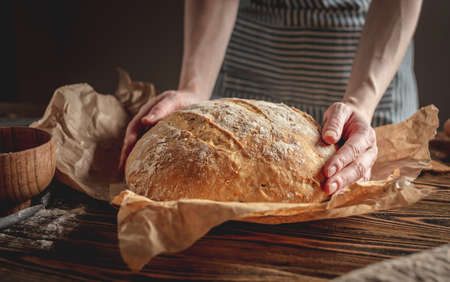 Female hands holding homemade natural fresh bread with a Golden crust on a napkin on an old wooden background . The concept of baking bakery products. rustic style.の写真素材