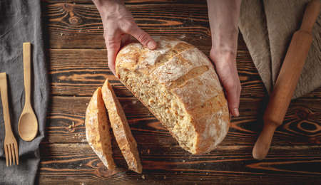 Female hands holding homemade natural fresh bread with a Golden crust on a napkin on an old wooden background . The concept of baking bakery products. rustic style.の写真素材