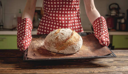 Female hands holding homemade natural fresh bread with a Golden crust on a napkin on an old wooden background . The concept of baking bakery productsの写真素材