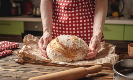 Female hands holding homemade natural fresh bread with a Golden crust on a napkin on an old wooden background . The concept of baking bakery productsの写真素材