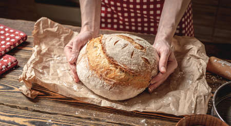 Female hands holding homemade natural fresh bread with a Golden crust on a napkin on an old wooden background . The concept of baking bakery productsの写真素材