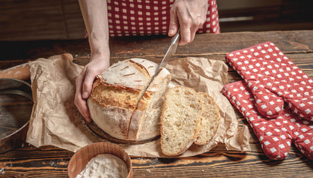 Women's hands cut with a knife homemade natural fresh bread with a Golden crust on a napkin on an...