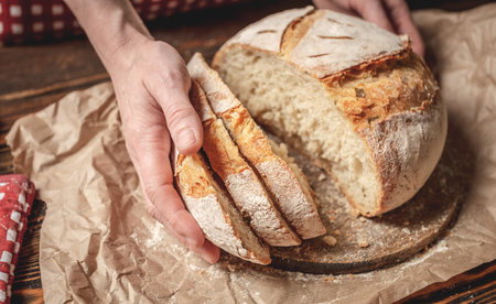 Women's hands cut with a knife homemade natural fresh bread with a Golden crust on a napkin on an...