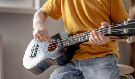 Cute funny boy is playing ukulele guitar in the music room. Joyful learning to play musical...