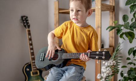 Cute funny boy is playing ukulele guitar in the music room. Joyful learning to play musical instruments.の写真素材