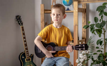 Cute funny boy is playing ukulele guitar in the music room. Joyful learning to play musical instruments.の写真素材