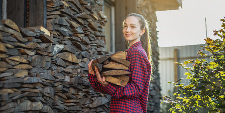 A woman is putting wood in hands from a woodpile for a home fireplace. The concept of wood-burning heating and the energy crisisの写真素材