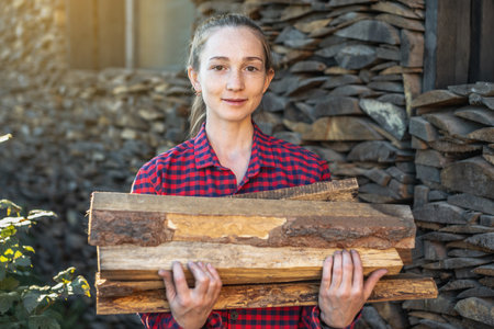 A woman is putting wood in hands from a woodpile for a home fireplace. The concept of wood-burning heating and the energy crisisの写真素材