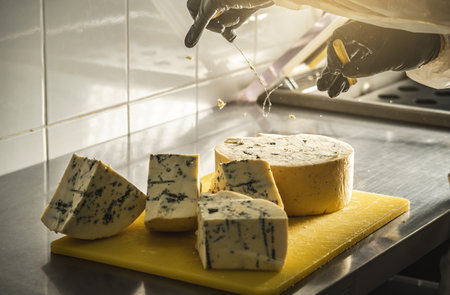 A farmer in black gloves cuts a head of spicy gorgonzola cheese with blue mold with a slicer into pieces.の写真素材