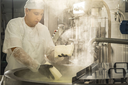 A man is a cheese maker in the process of producing different varieties of cheese in the industry. Concept of natural milk cheese making as a businessの写真素材