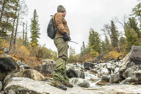 A tourist-traveler with a backpack stands in front of a mountain river in an autumn forest. The concept of freedom and unity with natureの写真素材