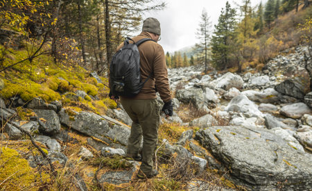 A tourist-traveler with a backpack stands in front of a mountain river in an autumn forest. The concept of freedom and unity with natureの写真素材