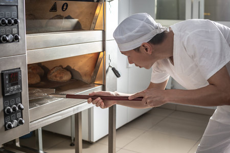 The baker is a man in the process of baking bread. Production of bakery products as a small...