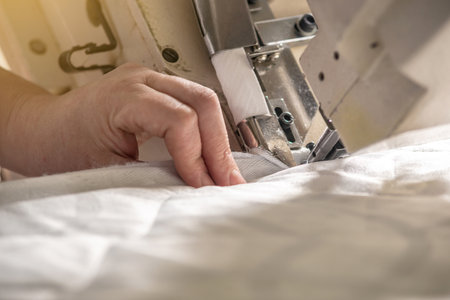 Women's hands in the process of sewing on professional equipment. Sewing fabric in production. Close-up.の写真素材