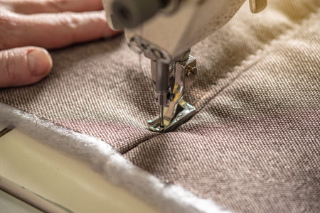 Women's hands in the process of sewing on professional equipment. Sewing fabric in production....